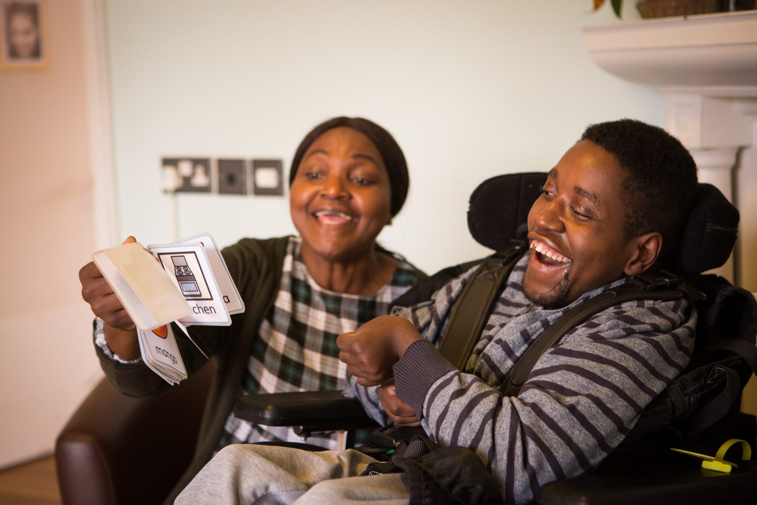 A woman reading words from visual cards to a young man in a wheelchair