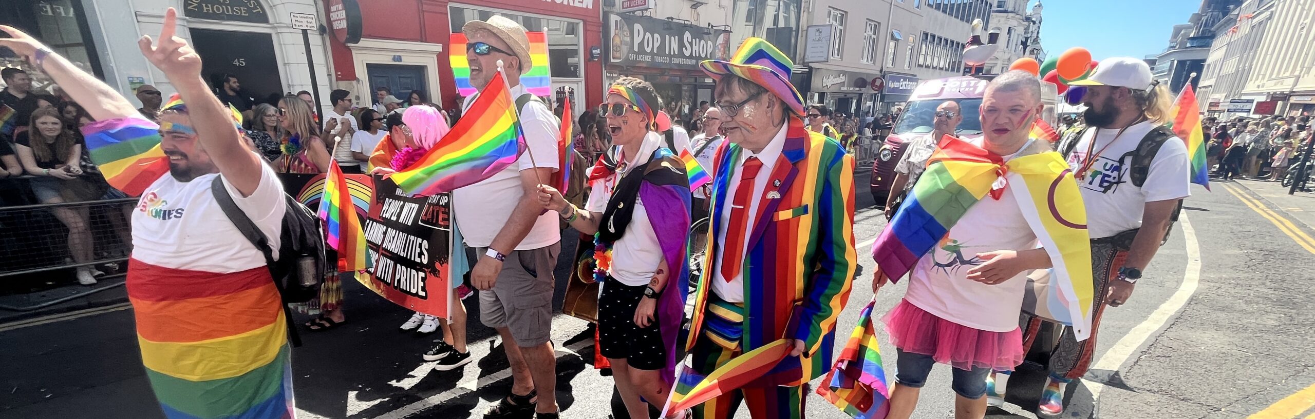 Image of people wearing rainbow flags and walking in a Pride Parade in Brighton