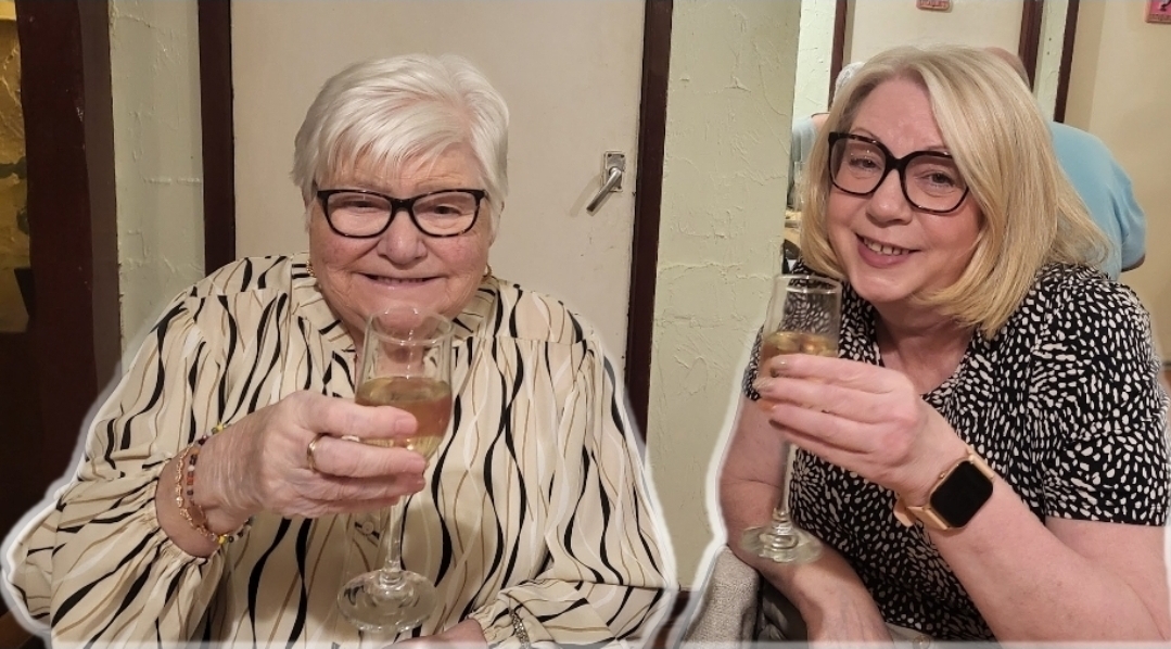 Julie and her mum Julie's mum, with blond hair and glasses holds up a glass of wine in a restaurant, alongside Julie, who is also holding up a glass of wine, both living their best life